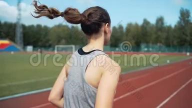 阳光明媚的日子里，年轻女子在体育场跑道上跑步